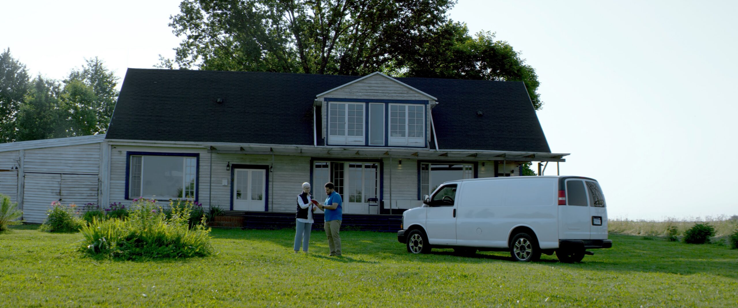 Homeowner signing paperwork with a home services professional beside a white service van at a residential property